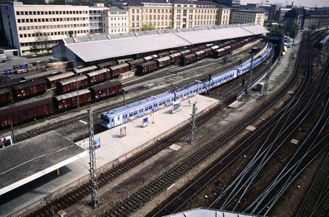 Überblick über den S-Bahnhaltepunkt und eine der beiden Güterhallen mit den zweiachsigen Güterwagen aus den 1960er-Jahren, im Jahr 1993. 420er-Triebwagenzug in der damaligen Flughafen-Farbgebung.