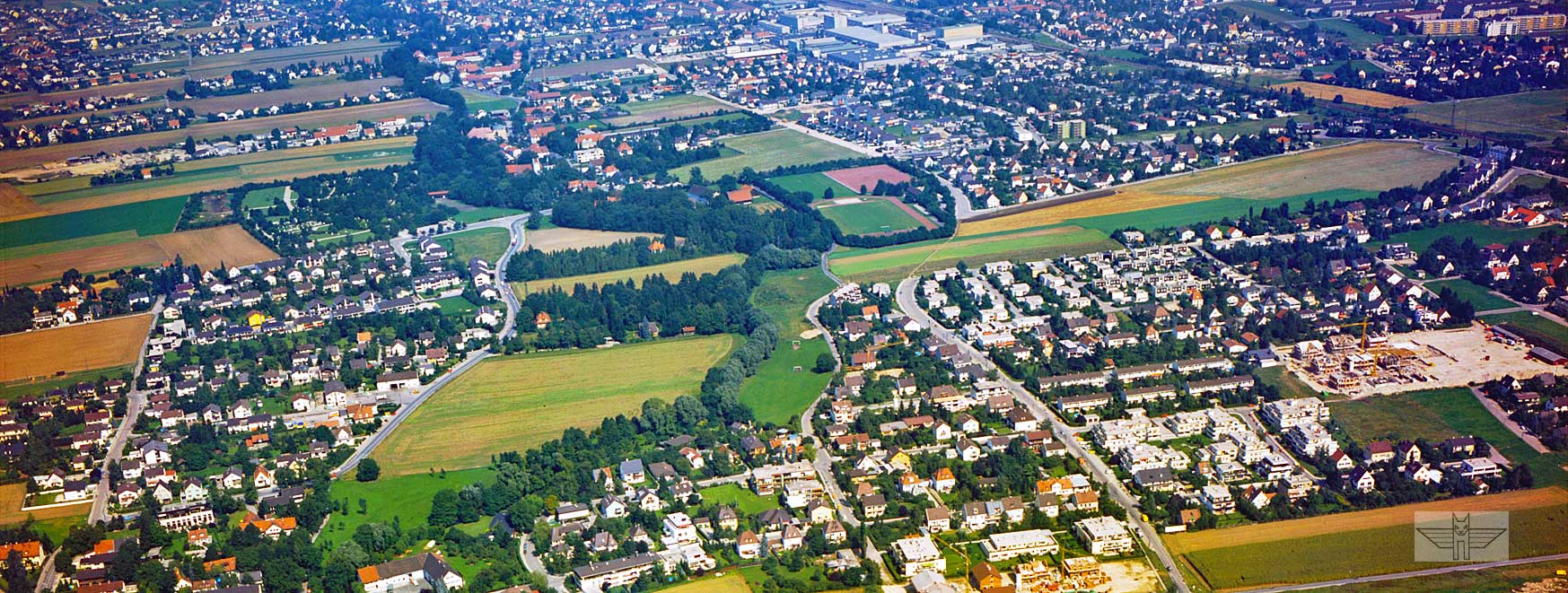 Blick auf die Von-Kahr-Straße. Bildmitte beginnend, zieht die etwas breiter ausfallende Wöhlerstraße vom unteren Bildrand bis zum Feld, und schwenkt dort zur rechten Seite in die Straße Im Wismat über. Direkt gegenüber der Wöhlerstraße sind die Grünanlagen entlang der Würm zu erkennen, die sich bis zur Von-Kahr-Straße selbst, und weiter entlang der Eversbuschstraße erstrecken. Am rechten Bildrand verläuft die Bahntrasse nach Moosach. Foto: K. Schillinger, 1979.